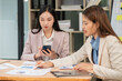 © Thitisak - Two Asian businesswomen holding graph papers are sitting and talking happily while working.