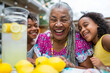 © Olha Havelia - Latina grandmother laughing while preparing cold lemonade at outdoor table with grandchildren,