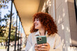 © Westend61 - Student with curly red hair smiling while holding a smartphone on a university campus