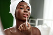 © fotofabrika - Woman applying lip gloss in a beauty routine at home during the daytime with natural light illuminating her face