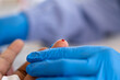 © InveStock - Close-up of a healthcare worker in blue gloves holding a patient's finger with a drop of blood during a medical examination or diagnostic blood test procedure.
