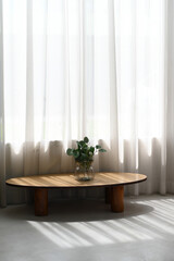 Aufkleber - Modern wooden oval coffee table stands beneath bright window veiled by sheer white sheer curtain, featuring glass vase with lush green plant, bathed warm sunlight casting long  shadow