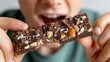 © Winter KD - Close-Up of Person Holding Chocolate Bar with Nuts and Crystals Showing Excitement and Enjoyment in a Relaxed Indoor Setting