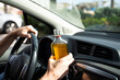 © vfhnb12 - Man holding a bottle of alcohol while driving a car, highlighting the danger and irresponsibility of drinking and driving.
