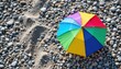 © Namwan - small colorful umbrella on gray pebbled beach travel lifestyle scene minimal summer accessory flat lay vacation mood simple outdoor coastal composition