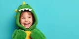 Happy child wearing plush dinosaur costume on solid background.