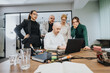 © qunica.com - A collaborative meeting where five colleagues gather around a laptop to discuss and analyze data in a modern office environment.