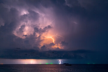 Wall Mural - Powerful cumulonimbus clouds with flashes of lightning peals of thunder over the ocean in the distance dark night