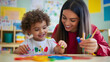© Ekaterina Pokrovsky - A caring pre-K teacher helping a young child paint with bright colors, sitting at a small table in a kindergarten classroom