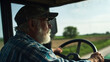© Sajib - A senior farmer driving a tractor with a white beard wearing a cap and a blue plaid shirt outside