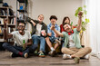 © Lomb - Group of diverse young friends cheering and eating popcorn together during a fun living room movie night