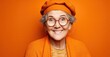 © Stock Pix - Smiling senior woman in an orange beret with matching cardigan. The woman's hair is gray, and she wears round glasses. Cheerful portrait.