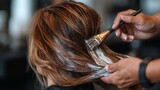 A woman with blonde hair is getting her hair done by a stylist. The stylist is using a brush to apply a product to the woman's hair. The woman is relaxed