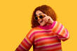 © GREGORIO - Cheerful redhead woman lowering sunglasses and smiling on yellow background