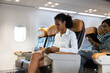 © NVB Stocker - Happy Woman traveling by plane and Write notes while traveling  in airplane. African American business female sitting in airplane during flight in first class seat