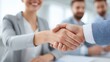 © Leninya - A professional handshake between business people signifies agreement and collaboration, with smiling individuals in the background.