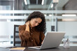 © Liubomir - A woman with curly hair, working on a laptop, massages her neck in pain, likely from strain.