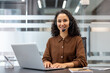 © Liubomir - A smiling customer service representative wearing a headset in a modern office setting, using a laptop at a desk.