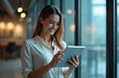 © miss irine - Businesswoman uses tablet in office near large windows. Happy woman reads news or communicates online, smiles. Modern tech, digital device, internet, social media.