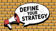 © shah - Megaphone with define your strategy speech bubble against a brick wall background