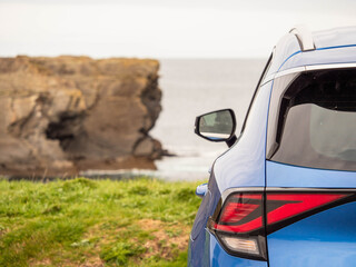 Wall Mural - A blue car is parked on the side of a road next to a cliff overlooking the ocean. Travel and tourism. Trip to nature, cloudy day, rough stone coast. Sightseeing landmarks. West of Ireland.
