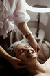 © Максим Галінский - A cosmetologist performs a beauty procedure on the head and face of a young woman.