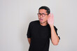 © KrishnaTedjo - Adult Asian man listening something with hand on his ear showing worried expression