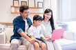 © Q88 - A happy family sitting on a couch watching a laptop together in their living room smiling