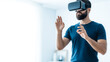 © mine95 - Man wearing a virtual reality headset with hands outstretched in a bright room.