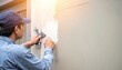 © Natty - A focused man wearing a blue shirt and a matching hat diligently repairs a textured wall, using tools and materials to ensure a sturdy finish.
