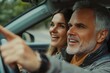 © Aara - Happy middle aged man pointing with finger at the road and saying something while woman driving car, enjoying trip together