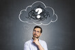© Who is Danny - Thoughtful man standing against dark wall background with a drawn cloud containing a question mark symbolizing confusion or curiosity.