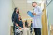 © Prapol Srinakara - sick african business woman sitting on wheelchair at corridor with asian woman assistant,getting service at examine room in hospital