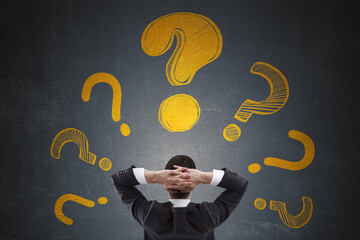 Fototapete - Businessman from rear view thinking with multiple large yellow question marks on dark background symbolizing confusion and decision making concept.