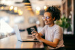 © Dusan Petkovic - Cheerful interracial remote worker sitting in cafe with laptop in front of her and texting messages.