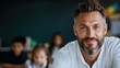 © Lazar - A cheerful male teacher with a beard smiles warmly in a classroom setting, embodying approachability, engagement, and the joy of learning for children in the background.