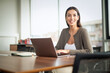 © gzorgz - Brunette haired middle aged woman sitting at desk in a modern office and using her laptop