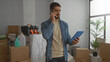 © Krakenimages.com - Young man holding tablet while talking on phone in new home with boxes in background implying unpacking and multitasking in bright living room setting