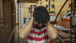 © Krakenimages.com - Young man with beard at construction site outdoors appears stressed holding head with hands in frustration wearing striped shirt surrounded by scaffolding in urban environment.