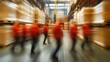 © At My Hat - Blurred warehouse workers in red uniforms walking by tall shelves. Illustrates fast-paced logistics, efficiency, movement, or industry.