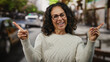 © Krakenimages.com - Woman smiling outdoors on a city street signals with hands in front of traffic during a sunny day wearing glasses and curly hair.
