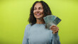 © Krakenimages.com - Middle-aged woman holding brazilian real banknotes while smiling against an isolated yellow background, embodying financial success and happiness.