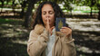 © Krakenimages.com - Middle-aged woman holding canadian passport while gesturing silence in a park setting, wearing a beige coat in an outdoor environment with trees in the background.