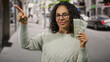 © Krakenimages.com - Middle-aged woman holding american dollars outdoors on a city street, confidently pointing in a direction, showcasing financial success and positivity.