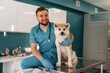 © standret - Sitting and smiling. Male veterinarian is with Akita Inu dog in clinic