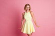 © deagreez - Young woman in a yellow dress smiling joyfully with a pink background highlighting her fashionable and charming look