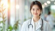 © Sirada - the young asian doctor is wearing a white coat and stethoscope around their neck, standing confidently in a brightly lit hospital hallway