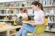 © JackF - Thoughtful woman reads books in the lecture hall. Female student is sitting in the library against the background of other students, she is looking for material for a diploma