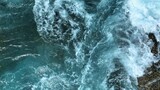 In slow motion, the ocean erupts against the rocks in an epic display of water and foam, capturing the vastness and unstoppable energy of the ocean as it collides with the shore.
