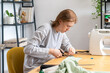 © Basil Pind/Stocksy - Teenager cutting fabric at table with sewing machine